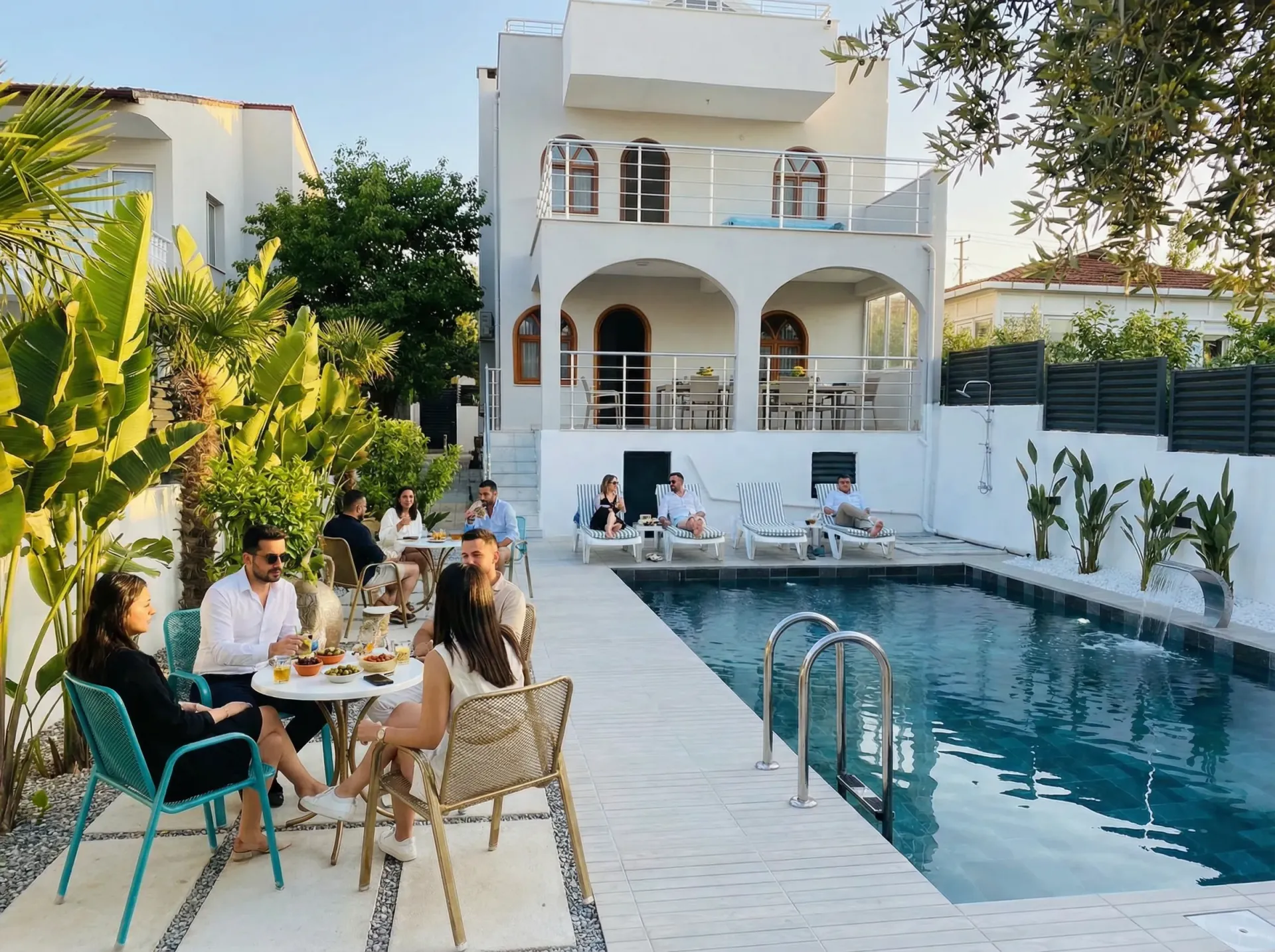Guests dining at tables by the pool at Villa Öz during a warm afternoon